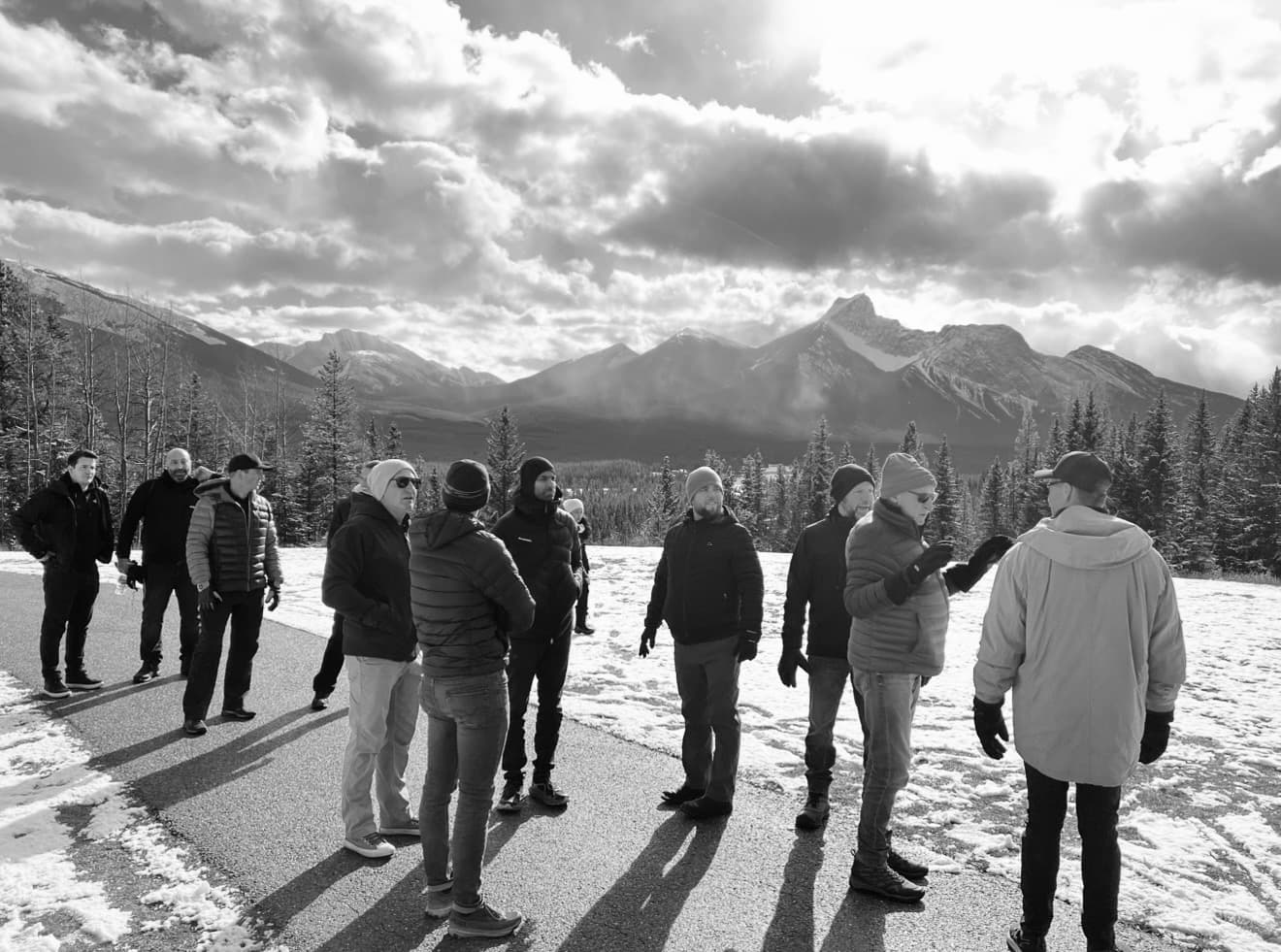 Men in winter gear stand on a snowy path with a dramatic mountain range behind.